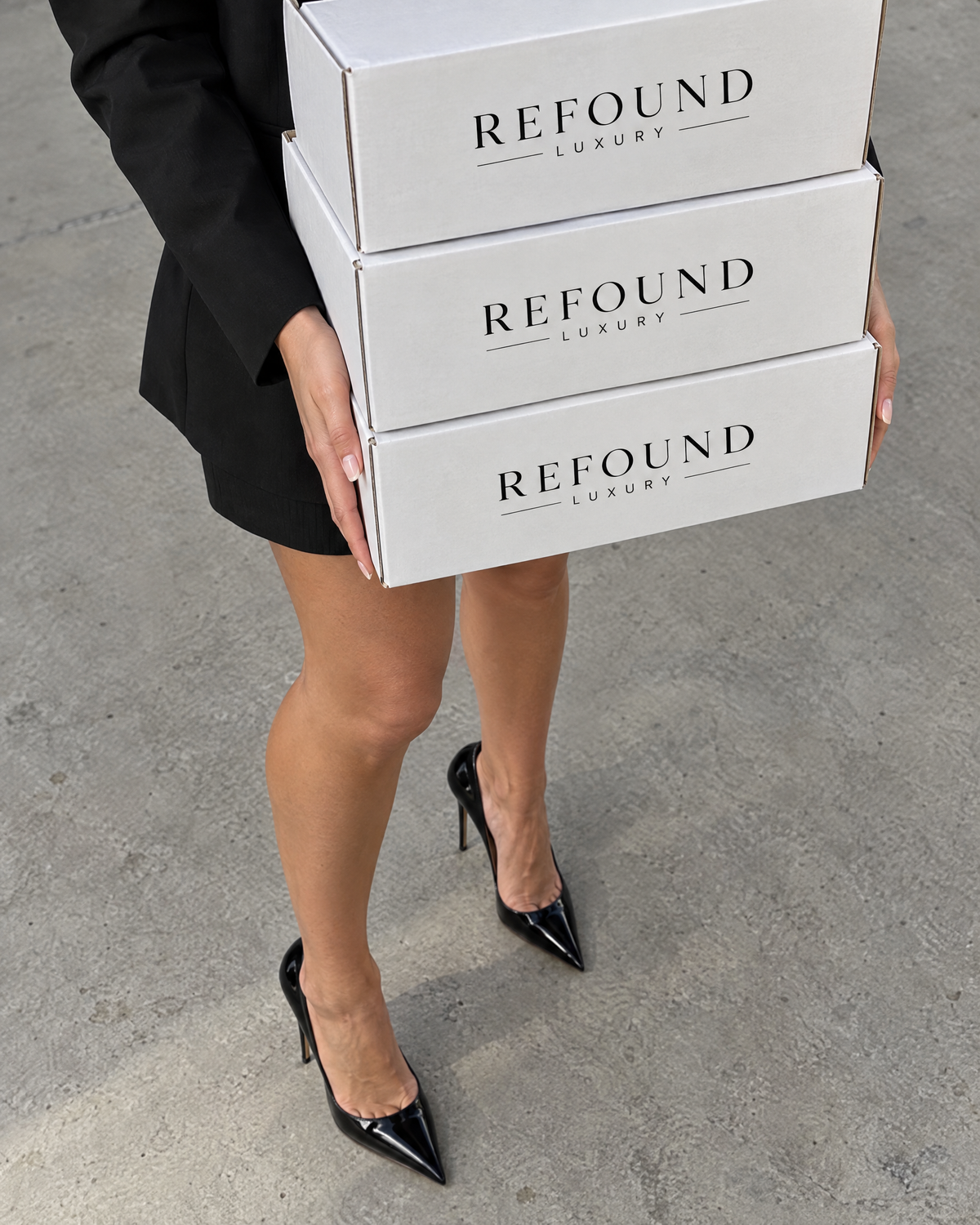 A woman in black heels carrying a stack of white Refound Luxury boxes