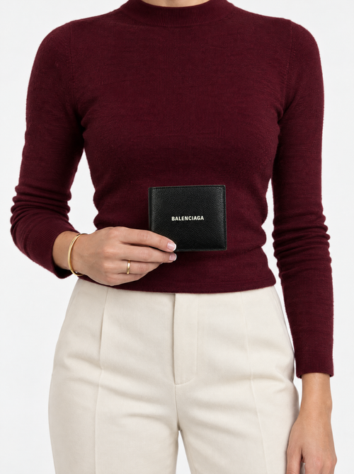Styled photo of the Balenciaga black bifold wallet held by a model